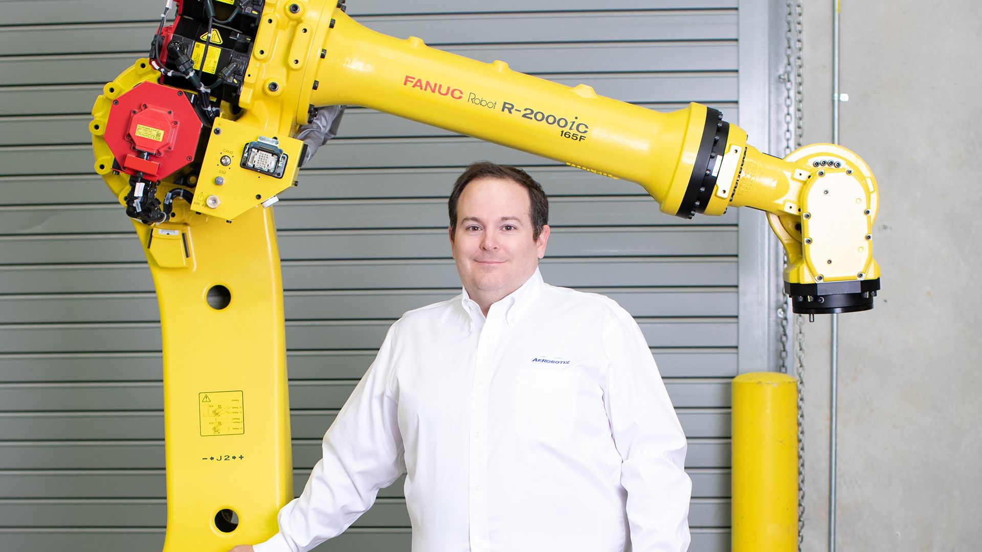 Josh Tuttle, business development manager at Aerobotix, poses in front of a FANUC robot. Tuttle was selected as 2024 Top 40 Under 40 by the Huntsville Business Journal.