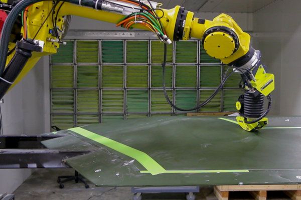 The automated Active Taping Kit applies a layer, using a FANUC robot arm, of green masking tape on a wing mold.